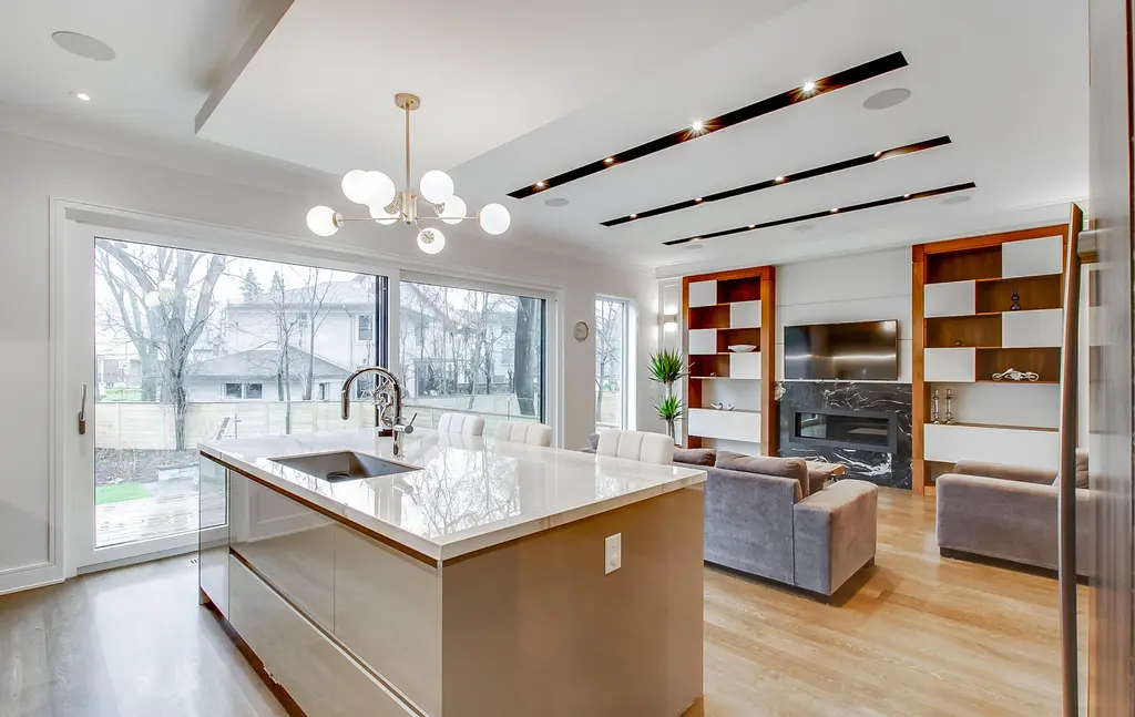 Modern open-concept kitchen and living room featuring a marble island, fireplace, and custom built-in shelving.